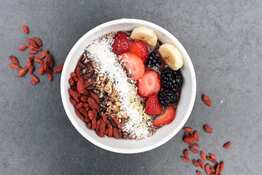 Strawberries, blackberries, bananas, grains and almonds in a white bowl on a gray background. 